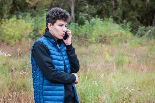 Adolescent Boy Calmly Talking On The Phone With His Parents While Walking In The Park, They Recently Learned To Solve Teenage Problems Together