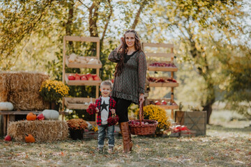 Fototapeta premium Young pregnant woman with long hair posing with her little cute son at the open market place. Fall background.