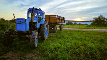 blue tractor with a trailer in a field on a summer evening