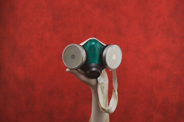 Respirator with replaceable filters. protection against respiratory threats. hand in a medical glove holds protective mask on a red background