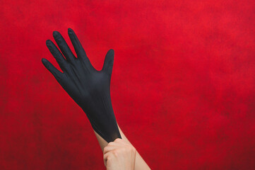 Hands in black medical gloves. person puts on surgical gloves on a red background