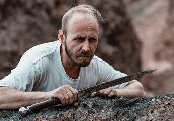 Warlike wanderer in the mountains resting after a battle with a dagger in his hand