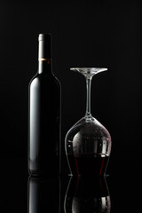 Bottle of red wine and an inverted glass with wine on a black background.