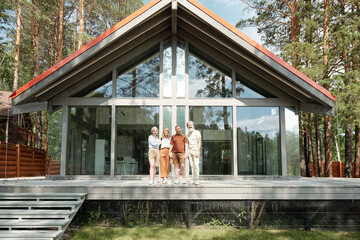Portrait of senior parents and their children standing against beautiful glass house while resting together in country