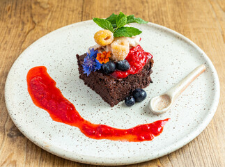 Gluten-free brownie with fresh organic fruit and a strawberry sauce. Tasty allergen-free dessert on a handmade ceramic plate. Chocolate brownie dessert.