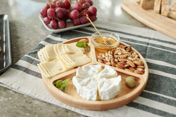 Close-up of various cheeses and nuts snacks on wooden plate placed on dining table with napkin