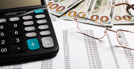 A calculator, cash and glasses lie on the table on the reports. Financial concept