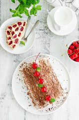 Homemade cake with cherries, sour cream and chocolate on a white plate on a wooden background. Vertical, copy space.