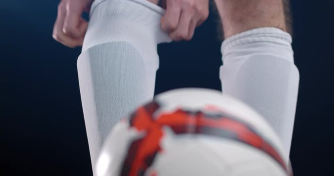 Footballer soccer player in boots putting his leg on a ball, black background. 4k