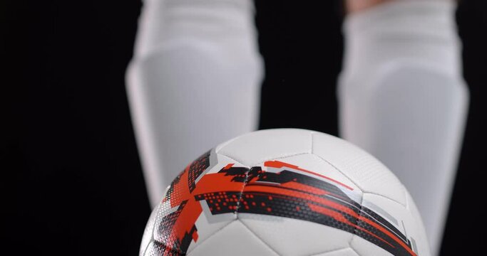 Footballer soccer player in boots putting his leg on a ball, black background. 4k
