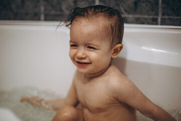 selective focus, noise effect: family is washing and bathing the baby in the bathroom, child girl have fun, she is happy and smiling, likes to enjoy water