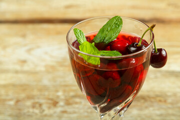 Crystal glass with cherry juice and fresh berries and mint inside on a wooden table.