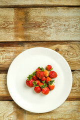 Fresh ripe strawberry on a white plate on a wooden table.
