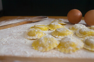 Homemade Ravioli / Tortellini /dumplings, preparing, cooking with two eggs , wooden spoon and rolling pin,on floured wood.Close up view of homemade pasta concept.Black background.
