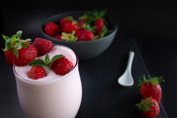 Delicious strawberry smoothie or milkshake glass with fresh strawberries in a bowl ,a white spoon ,on a slate dark background.(Healthy food/drink concept).
