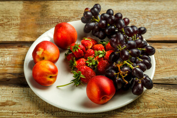 Grapes and peaches and strawberries on a wooden table.