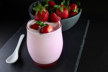 Milkshake / strawberry smoothie  glass with fresh strawberries in a bowl ,a white spoon ,on a slate dark background.(Healthy food/drink concept).