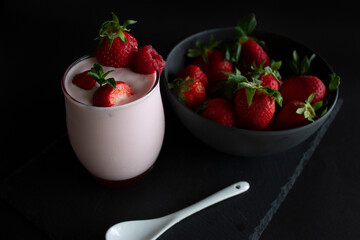 Delicious strawberry smoothie or milkshake glass with fresh strawberries in a bowl ,a white spoon ,on a slate dark background.(Healthy food/drink concept).