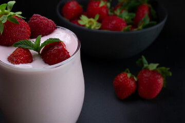 Strawberry smoothie or milkshake glass with fresh strawberries in a bowl ,on a slate dark background.(Healthy food/drink concept).