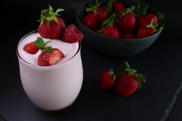 Strawberry smoothie or milkshake glass with fresh strawberries in a bowl,on a slate dark background.(Healthy food/drink concept).