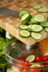 Cook holds knife in hand and cuts on cutting board green cucumber for salad or fresh vegetable soup with vitamins. Raw food and vegetarian recipe book in modern society popular concept.
