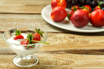 Strawberries in a cup with whipped cream on a table near fruits.