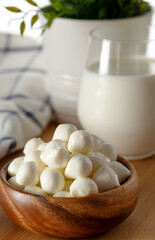Mozzarella cheese balls in bowl and glass of milk on wooden background