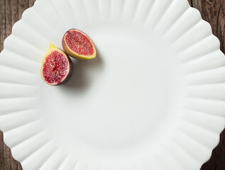Halves figs on a plate. Sliced fresh figs on a white plate on a wooden background. Top view. 