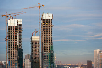 Fototapeta na wymiar High rise building under construction in evening sky and cloud. Under construction tall building ( skyscraper) with yellow construction cranes next to it. New luxury district. 