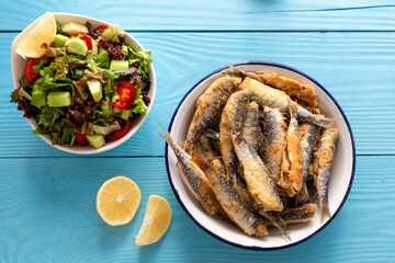 Fried sardines with lemon and salad on wooden background