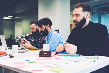 Crew of skilled IT professionals brainstorming working on creating program software during informal meeting using modern laptop computer and wireless connection to internet sitting at table in office