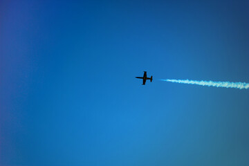 A plane flying over the blue sky background. Air show at Chisinau National Airport in Moldova. Airplane with dense decorative smoke behind.