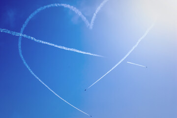 Three planes flying against the blue sky background, forming a dense smoke heart symbol. Airshow at Chisinau Airport in Moldova. Aircrafts with  decorative smog in the back. Entertainment concept.
