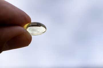 vitamin d, fingers holding capsule, with blue sky background.