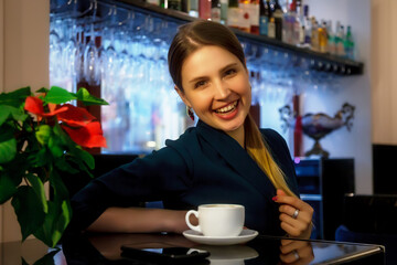 Girl of Slavic appearance in bar, cafe or restaurant with white Cup. Female shows emotion. Young charming woman is sitting at bar and drinking coffee or tea in her free evening time