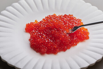 Appetizer red caviar on a white plate with a fork or spoon. Gourmet food, close up. Shallow depth of field