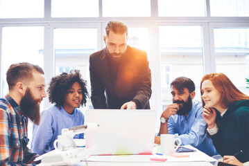 Fototapeta premium Handsome business coach showing to diverse group of students training webinar during lesson,professional male leader of working group presenting creative ideas watching video on laptop with colleagues