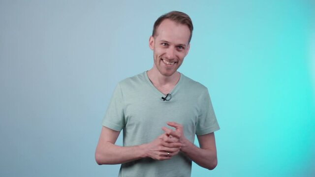 A young man on a turquoise background is talking to someone behind the camera and laughing. The microphone is attached to the t-shirt. Online training. Recording an online course