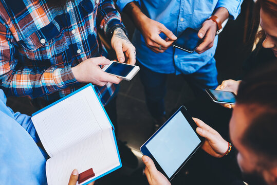 Group of skilled young male and female IT developers testing new software for digital devices using gadgets connected to free wireless internet in office while discussing advantages and disadvantages