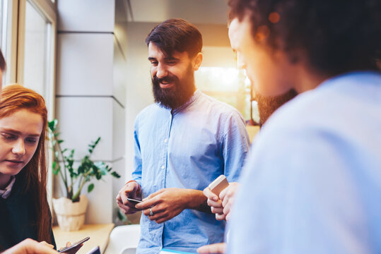 Crew of young skilled male and female IT developers communicating while having work break sharing thoughts about usability of smartphones installing application downloading from web store using wifi