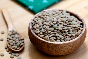 Green lentils in wooden bowl on wooden background.