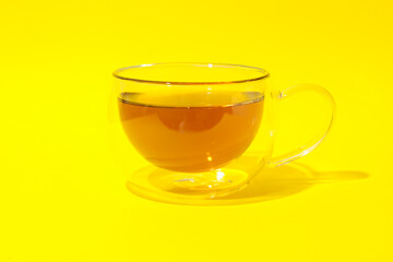 Glass cup of chamomile tea on yellow background