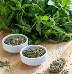 Dried peppermint in a white bowl and a bunch of fresh mint, on wooden background. Food background.
