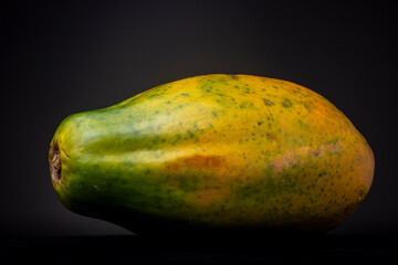 Large green, yellow and orange colourful fresh tropical red papaya fruit against a dark background. Studio low key food still life.