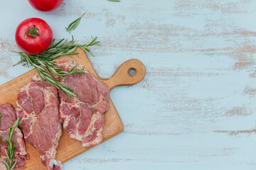 Raw fresh meat steak entrecote, tomatoes, rosemary and seasonings on cutting board.