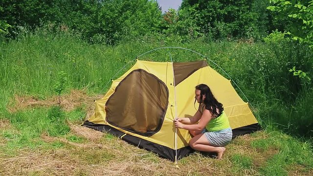 A man and a woman in a clearing put up a tent and attach a tent to the arche