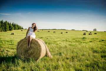 Naklejka na ściany i meble Beautiful girl is resting after work. girl on the field with hay. Woman near a sheaf of hay in a field. Rural life. Holidays in the village