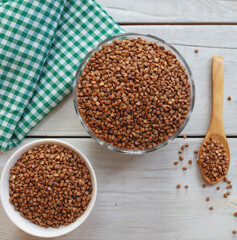 Bowl of raw buckwheat with spoon on wooden background