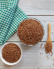 Bowl of raw buckwheat with spoon on wooden background