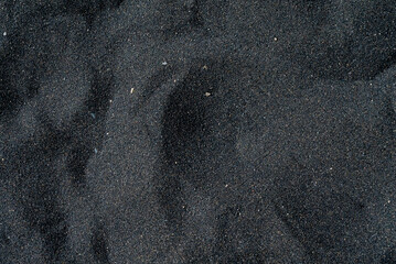 Black sand beach macro photography. Silky black beach texture. Minimalistic black background. Tenerife voulcanic sandy shore.